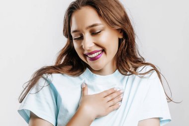 Kadın kendini işaret ediyor ve gülüyor. Güzel, kumral, uzun saçlı, moda makyajlı, mor dudaklı, izole gri arka planda güzel bir kız.