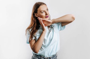 Güzel bir genç kız gülümser, hayal kurar ve ellerini yüzünün yakınında beyaz, ıssız, gri bir arka planda tutar. Reklam için yer var. Mor dudaklı, modaya uygun bir kadın..