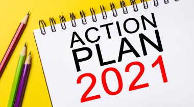 Aksiyon Planı 2021 sarı arka planda kalemleri olan beyaz bir not defterinde. İş konsepti