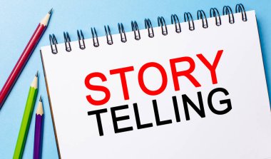 Mavi arka planda kalemler olan beyaz bir not defterine Storytelling yaz. İş konsepti