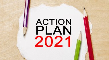 Ahşap bir arka planda kalemler olan beyaz bir not defterine Action Planı 2021 'i yaz. İş konsepti