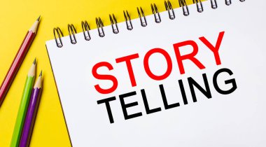 Beyaz bir not defterinde, sarı arka planda kalemler var. İş konsepti