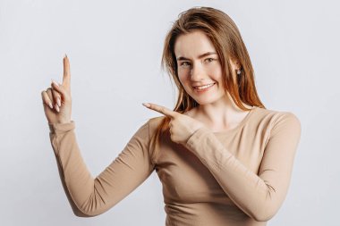 Güzel, genç, esmer kız gülümseyen ve parmaklarını yalıtılmış beyaz bir arka planda gösteren.