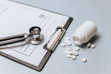 Beyaz haplar, steteskop, doktorun masasında reçete. Tıp konsepti. Tıbbi ürünlerin dozunu belirleme araştırması. Sağlık hizmeti ya da hastalık. Hastanede veya eczanede hap veya hap.