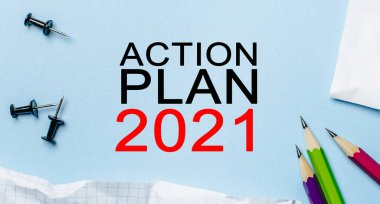 Mavi arka planda kalemleri olan beyaz bir not defterine Action Plan 2021 'i yaz. İş konsepti