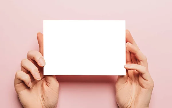 女性的手拿着一张粉红色背景的空白纸片 广告空间 — 图库照片