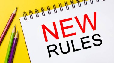 Sarı arka planda kalemler olan beyaz bir not defterine yeni kurallar yaz. İş konsepti