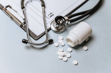 Beyaz haplar, steteskop, doktorun masasında reçete. Tıp konsepti. Tıbbi ürünlerin dozunu belirleme araştırması. Sağlık hizmeti ya da hastalık. Hastanede veya eczanede hap veya hap.