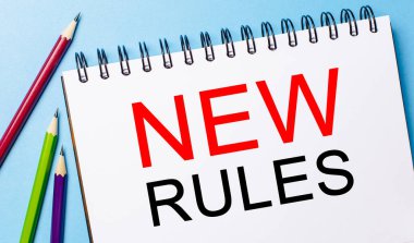 Mavi arka planda kalemler olan beyaz bir not defterine yeni kurallar yaz. İş konsepti