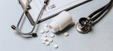Beyaz haplar, steteskop, doktorun masasında reçete. Tıp konsepti. Tıbbi ürünlerin dozunu belirleme araştırması. Sağlık hizmeti ya da hastalık. Hastanede veya eczanede hap veya hap.