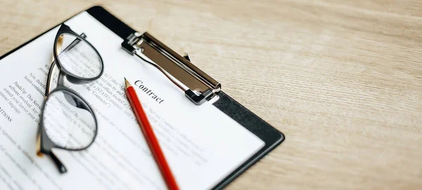 A contract on a wooden work table with glasses and a red pencil. The documents are ready for signing. Business concept. Collaboration agreement.