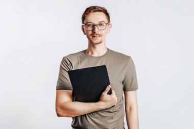 Evraklar için klasör tutan genç yakışıklı adam, öğrenci, işçi veri bilgilerine bakıyor, gri arka planda izole edilmiş fotoğraf için poz veriyor. Reklam için yer.