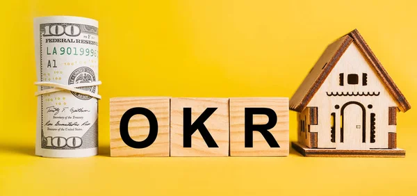OKR with house miniature model and money on a yellow background. Investment, real estate, home, housing, earnings, financial concept