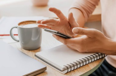 Adam iş yerindeki not defterine akıllı telefonuyla iş bilgileri yazıyor.