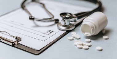 Beyaz haplar, steteskop, doktorun masasında reçete. Tıp konsepti. Tıbbi ürünlerin dozunu belirleme araştırması. Sağlık hizmeti ya da hastalık. Hastanede veya eczanede hap veya hap.