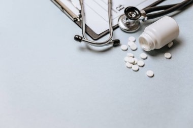 Beyaz haplar, steteskop, doktorun masasında reçete. Tıp konsepti. Tıbbi ürünlerin dozunu belirleme araştırması. Sağlık hizmeti ya da hastalık. Hastanede veya eczanede hap veya hap.