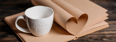 Kupa, aşk ve sevgililer günü konsepti ile ahşap bir masa üzerindeki kitap kağıtlarından yapılmış kalp.