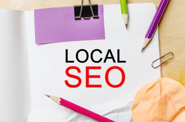 Ahşap bir arka planda kalemler olan beyaz bir not defterine SEO LOCAL mesajı gönder. İş konsepti