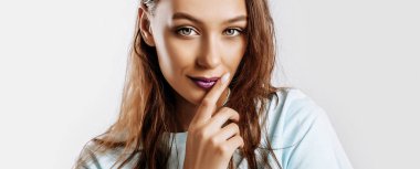 Güzel, tatlı esmer kız, uzun saçlı, moda makyajlı, mor dudaklı, izole gri arka planda. Kadın elini yüzüne dayadı ve kameraya baktı. Hoş bir model.