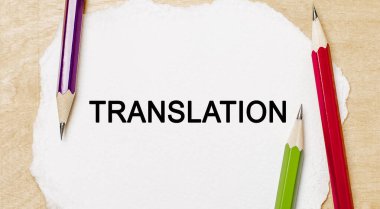 Tahta arka planda kalemler olan beyaz bir not defterine TRANSLATION metni yaz. İş konsepti