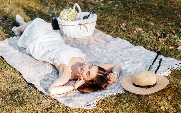 Baharda parkta hasır şapkalı pikniğe giden bir kız. Esmer, uzun saçlı, yaz doğasının arka planında bir ekose üzerinde yatıyor. Gençlik ve güzellik.