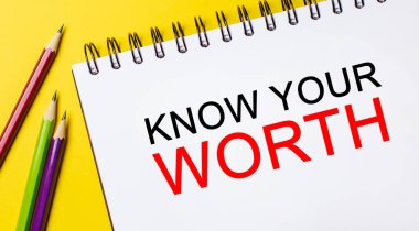 Sarı arka planda kalemler olan beyaz bir not defterindeki değerini bil. İş konsepti