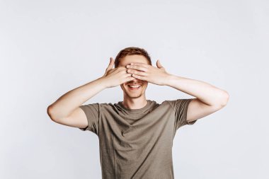 Yakışıklı genç adam gözlerini iki eliyle kapar ve gülümser. Yeşil gömlekli, gri arka planda poz veren esmer bir kadın. Reklam için yer var. Göremiyorum..