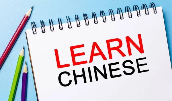 Learn Chinese on a white notepad with pencils on a blue background. Business concept