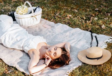 Baharda parkta hasır şapkalı pikniğe giden bir kız. Esmer, uzun saçlı, yaz doğasının arka planında bir ekose üzerinde yatıyor. Gençlik ve güzellik.