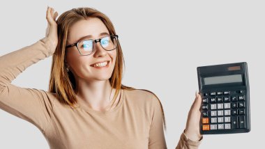 Gözlük takan genç ve güzel bir iş kadını gri arka planda hesap makinesi tutuyor. Kariyer zenginliği muhasebe konseptini başarıya ulaştırmak. Reklam için kapak