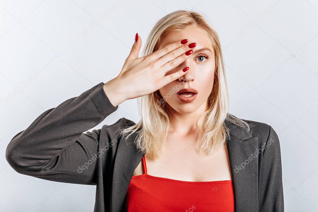 The blonde girl is surprised badly covers half of her face with her hand. The woman remembered, learned and understood important information about the business. Isolated background for advertising.