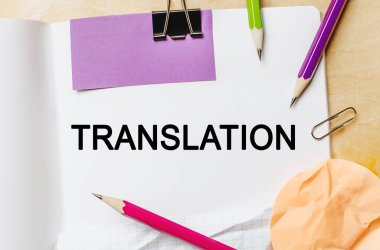 Tahta arka planda kalemler olan beyaz bir not defterine TRANSLATION metni yaz. İş konsepti