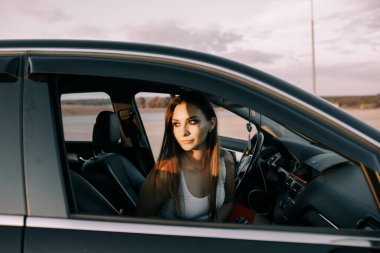 Gün batımında, boş bir otoparkta araba süren güzel bir genç kız.