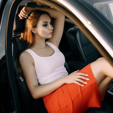 Güzel bir genç kız akşamları gün batımında arabada oturur. Yaz güneşi boş bir otoparkta.