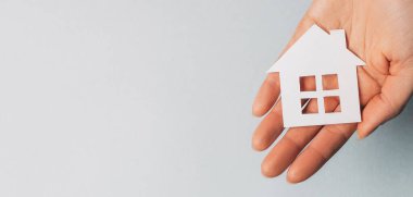 Açık mavi arka planda elleri güneşli kağıt bir ev tutan bir kadın. Güzel ev.