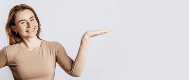 Güzel, genç, esmer bir kız gülümseyip elini yalıtılmış beyaz bir arka planda gösteriyor.