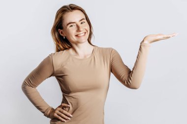 Güzel, genç, esmer bir kız gülümseyip elini yalıtılmış beyaz bir arka planda gösteriyor.