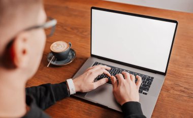 İş yerinde dizüstü bilgisayarda çalışan yakışıklı bir adam. İş adamı, çalışma masasındaki bilgisayarda kahve ile bilgi yazıyor.