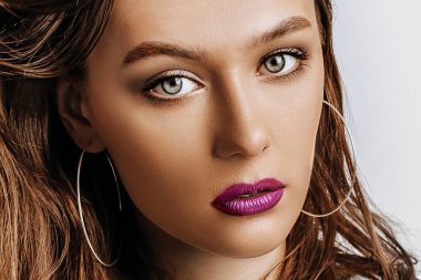 Güzel, genç, esmer, yeşil gözlü, uzun saçlı, moda makyajlı, mor dudaklı, izole gri arka planda bir kız. Kadın cidden kameraya bakıyor. Hoş bir model.