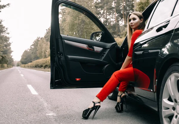 Piękna Młoda Dziewczyna Czerwonym Kombinezonie Siedzi Kierownicą Czarnego Samochodu Pustej — Zdjęcie stockowe
