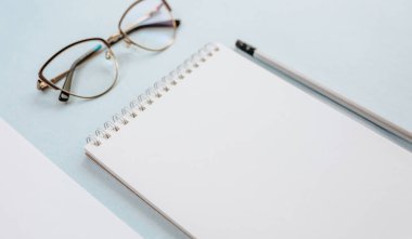 Ofis kavramı. Çalışma alanı gözlüklü, defterli ve kalemli. Boşluğu beyaz ve mavi olarak kopyala.