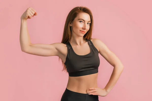 Spor kıyafetleri içinde pembe arka planda gülümseyen fitness kızı. Güzel atletik bir vücudu ve bronzlaşmış bir teni olan zayıf bir kadın.
