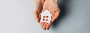 Açık mavi arka planda elleri güneşli kağıt bir ev tutan bir kadın. Güzel ev.