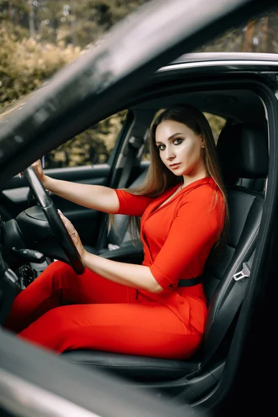 Una Hermosa Joven Con Mono Rojo Sienta Volante Coche Negro — Foto de Stock