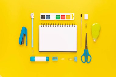 Modern beyaz, mavi, sarı ofis masaüstü, okul gereçleri ve kırtasiye malzemeleriyle dolu. Masanın etrafında mesaj için boş alan var. Okula dönüş konsepti dairesi modelle yatıyordu.
