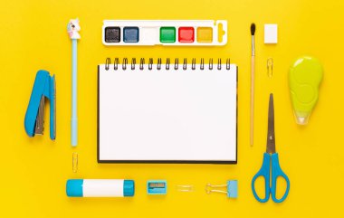 Modern beyaz, mavi, sarı ofis masaüstü, okul gereçleri ve kırtasiye malzemeleriyle dolu. Masanın etrafında mesaj için boş alan var. Okula dönüş konsepti dairesi modelle yatıyordu.