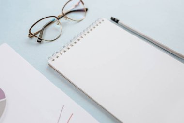 Ofis kavramı. Çalışma alanı gözlüklü, defterli ve kalemli. Boşluğu beyaz ve mavi olarak kopyala.