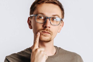 Gözlüklü, esmer sakallı genç yakışıklı adam. Öğrenci, işçi, iş adamı. Gri arka planda izole edilmiş fotoğraf için poz veriyorlar. Reklam için yer.