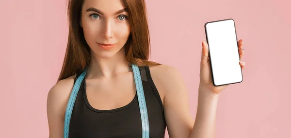 健康女孩笑着拿起电话 拿着一个模型 摆出一副粉红背景的黑色运动服的尺码 身材苗条 体形漂亮 皮肤晒黑的女人 — 图库照片