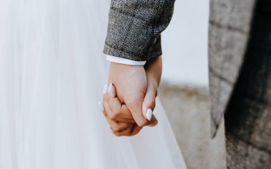 Gelin ve damat el ele tutuşuyor. Düğün gününde bir çift olarak.